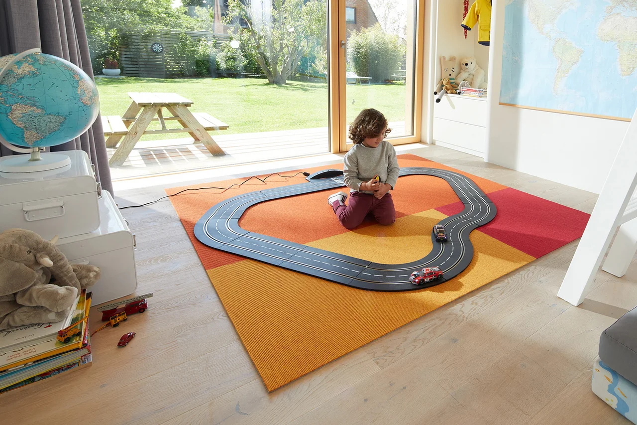 Ein Teppich liegt im Kinderzimmer. - Ein Teppich in fröhlichen Farben liegt im Kinderzimmer. Ein Kind spielt darauf mit einer Rennbahn.